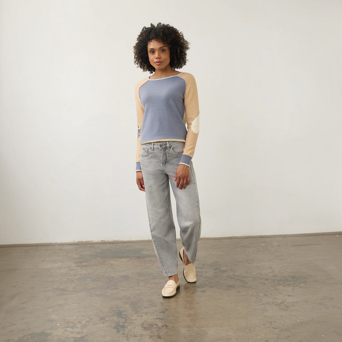 Model wearing Plum Bottom FDJ Girlfriend Barrel Ankle Jeans in light grey denim with a blue and beige sweater