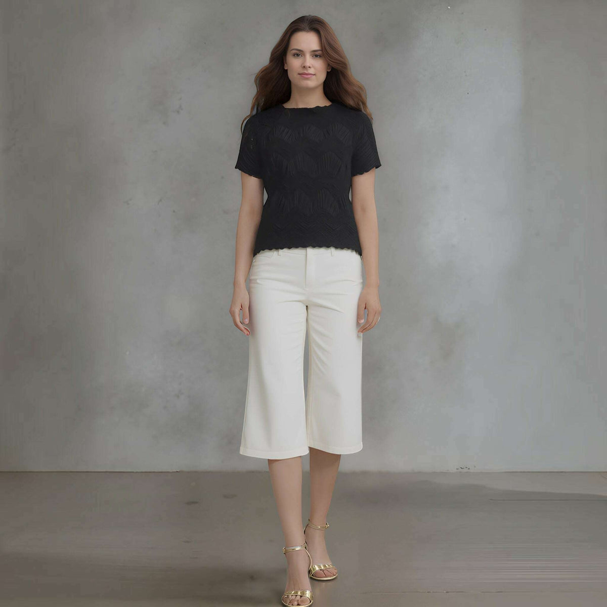Plum Bottom model wearing a black Ellyndale short-sleeve top with crochet wave pleating and white cropped trousers.