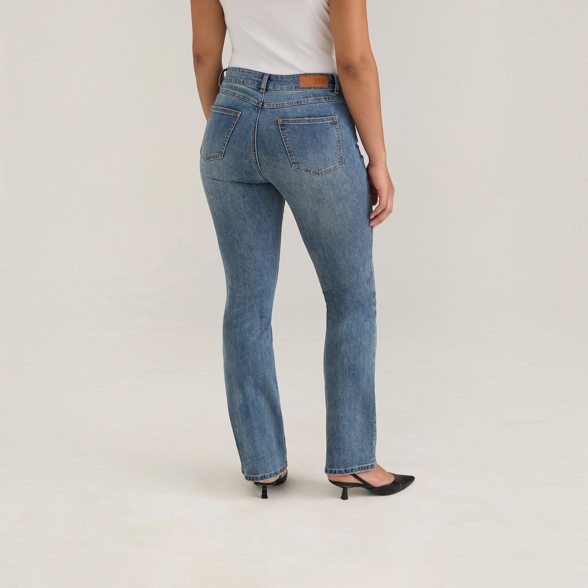 Plum Bottom FDJ Christina bootleg jeans in medium wash denim, shown from the back with a white top and black heels.