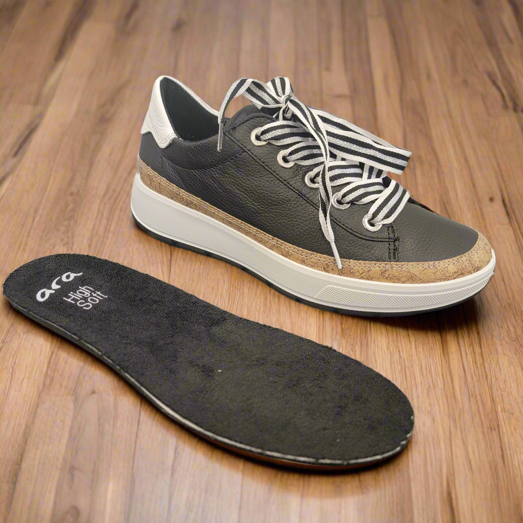 Black sneaker with white laces and a visible sole on a gray surface
