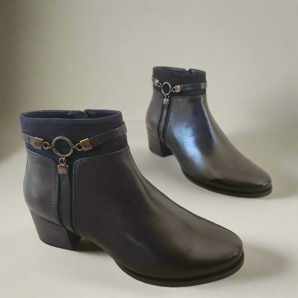 Pair of black leather boots with decorative rings on a beige floor.