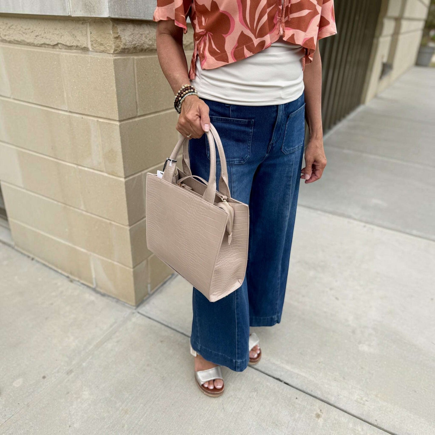 Plum Bottom SONDRA ROBERTS nude croc-embossed frame bag with dual handles held by a woman in casual attire.