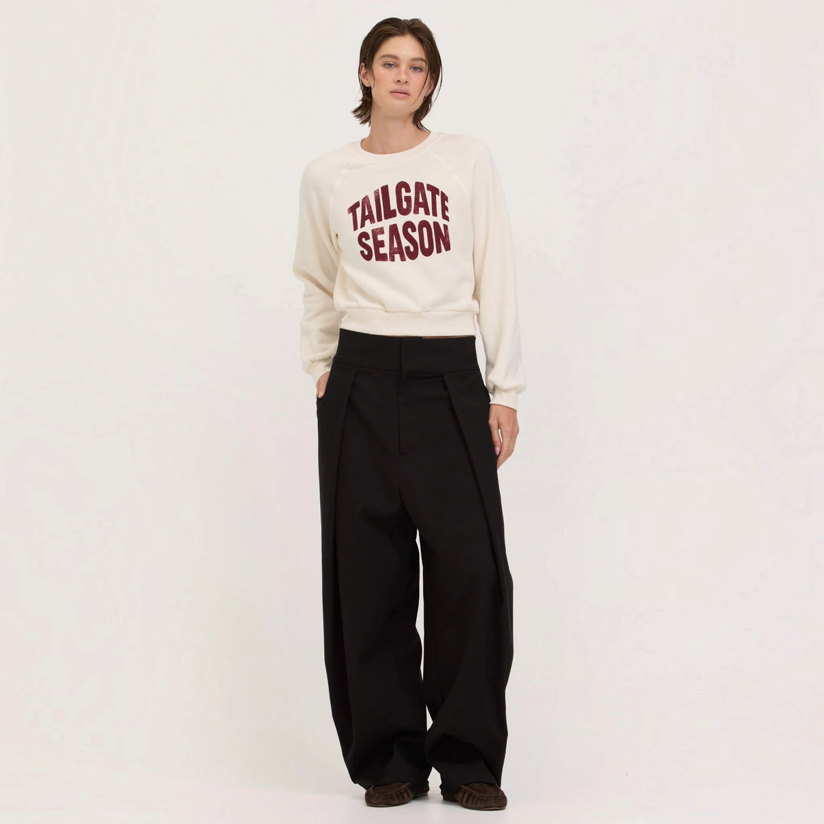 Plum Bottom PROJECT SOCIAL cream sweatshirt with Tailgate Season graphic worn by a model with black wide-leg trousers