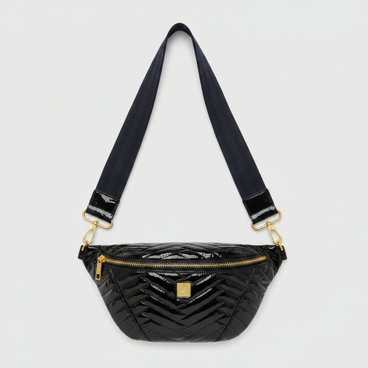 A glossy black chevron-patterned patent leather fanny pack with a wide navy blue strap and gold-tone hardware, resting on a beige fabric surface.