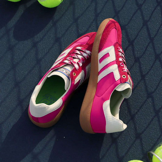 A pair of pink and white low-top sneakers styled on a dark tennis court with bright yellow tennis balls scattered around.