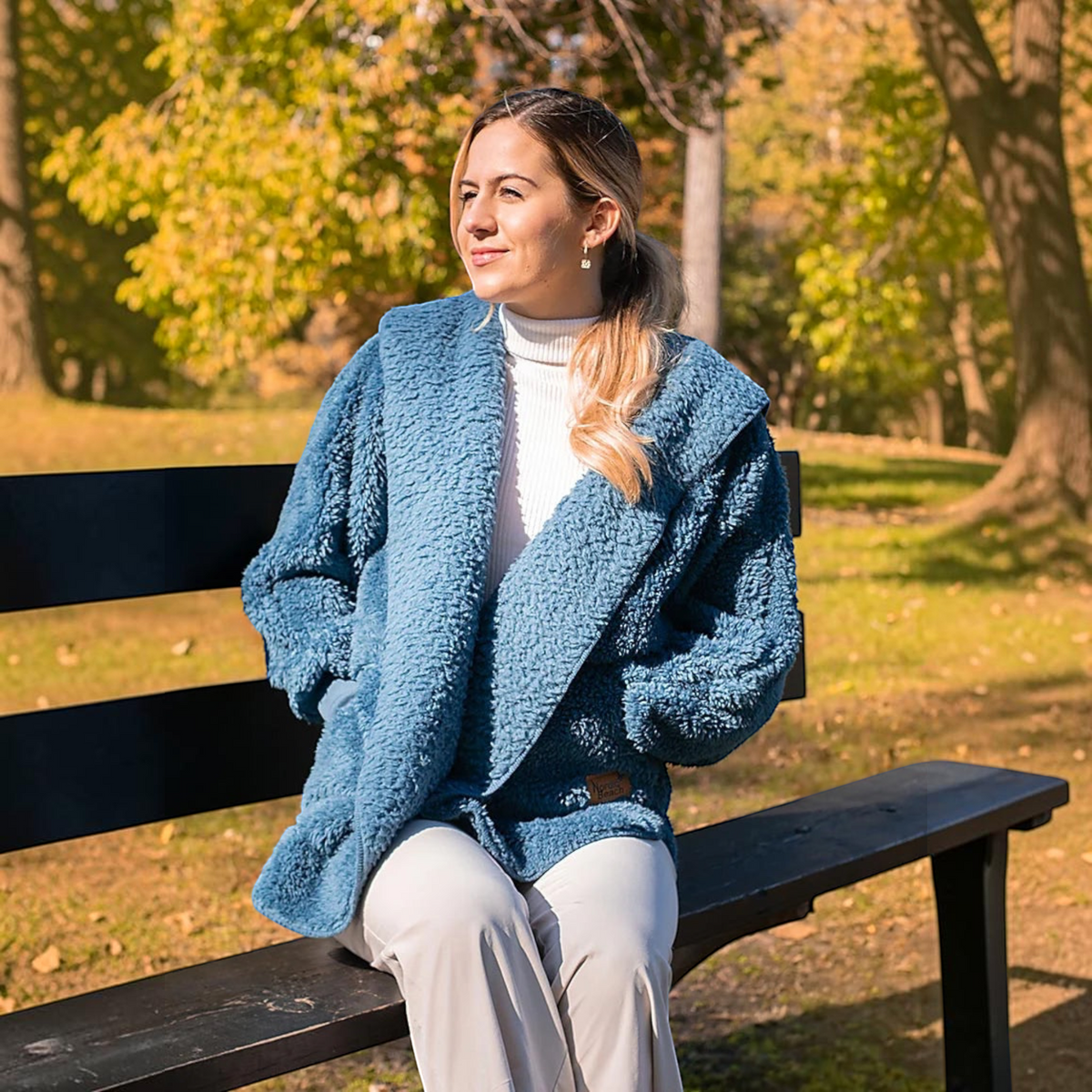 Plum Bottom NORDIC BEACH blue hooded body wrap jacket worn by a woman sitting on a park bench in autumn