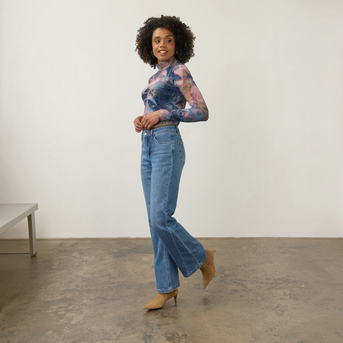 Model wearing Plum Bottom FDJ Olivia bootleg jeans in medium wash denim paired with a patterned mesh top and boots