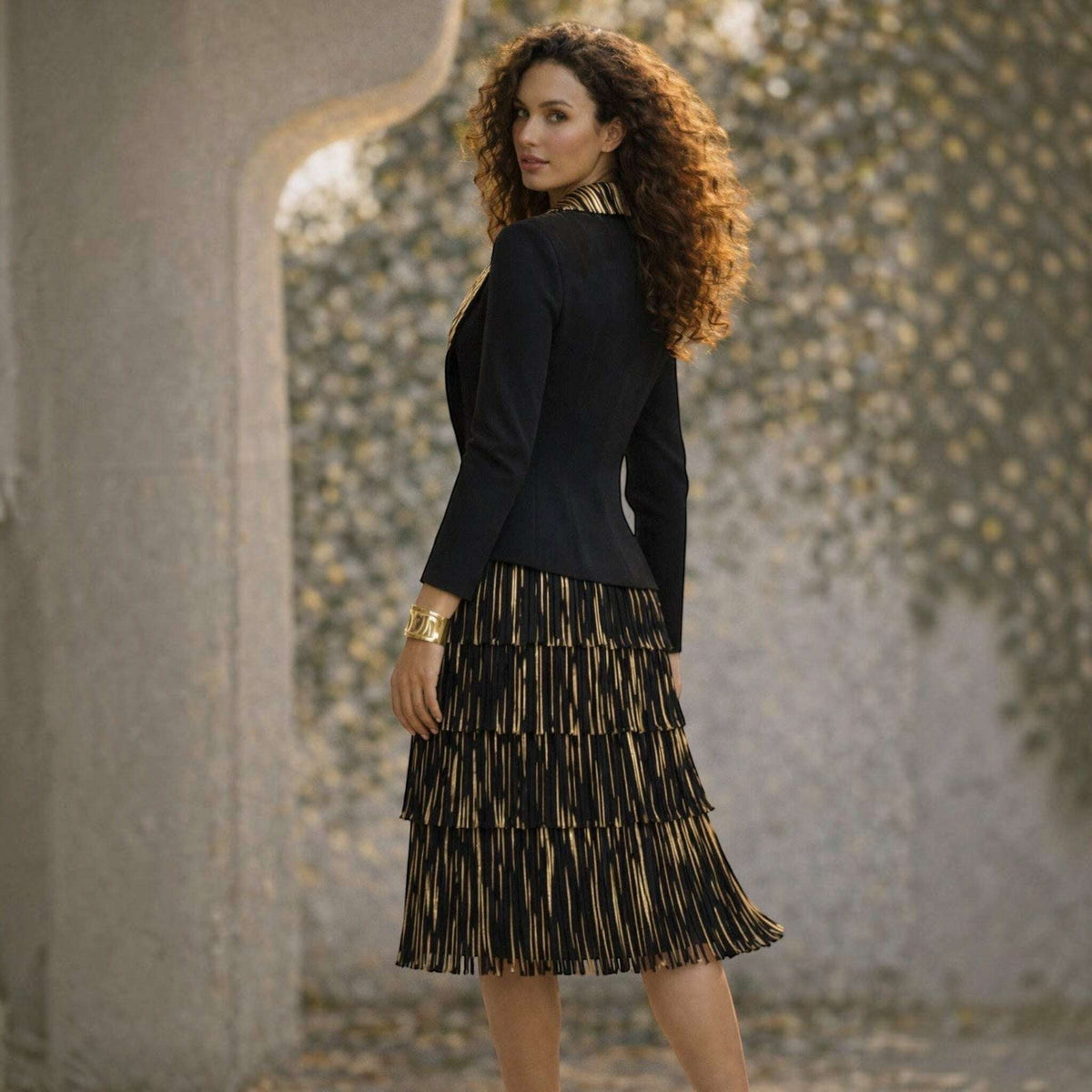 Plum Bottom Ellyndale black and gold pleated dress set with fringe trim and matching jacket on a curly-haired model