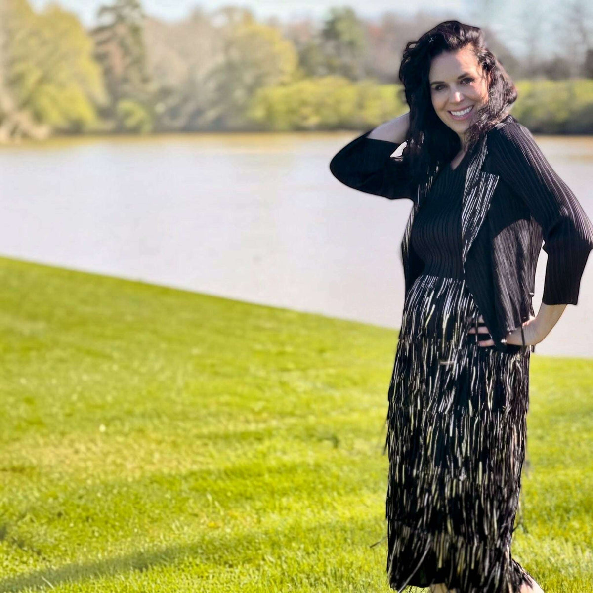 Plum Bottom Ellyndale black and gold pleated sleeveless dress and jacket set with fringe trim worn by a smiling woman