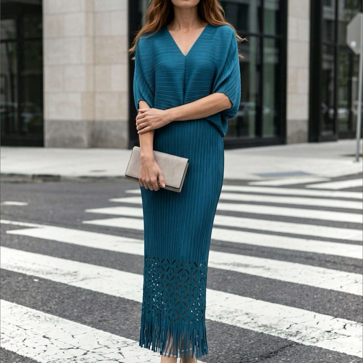 Plum Bottom teal pleated midi dress with waist cutout, laser-cut hem, and fringe detail worn on a city street.
