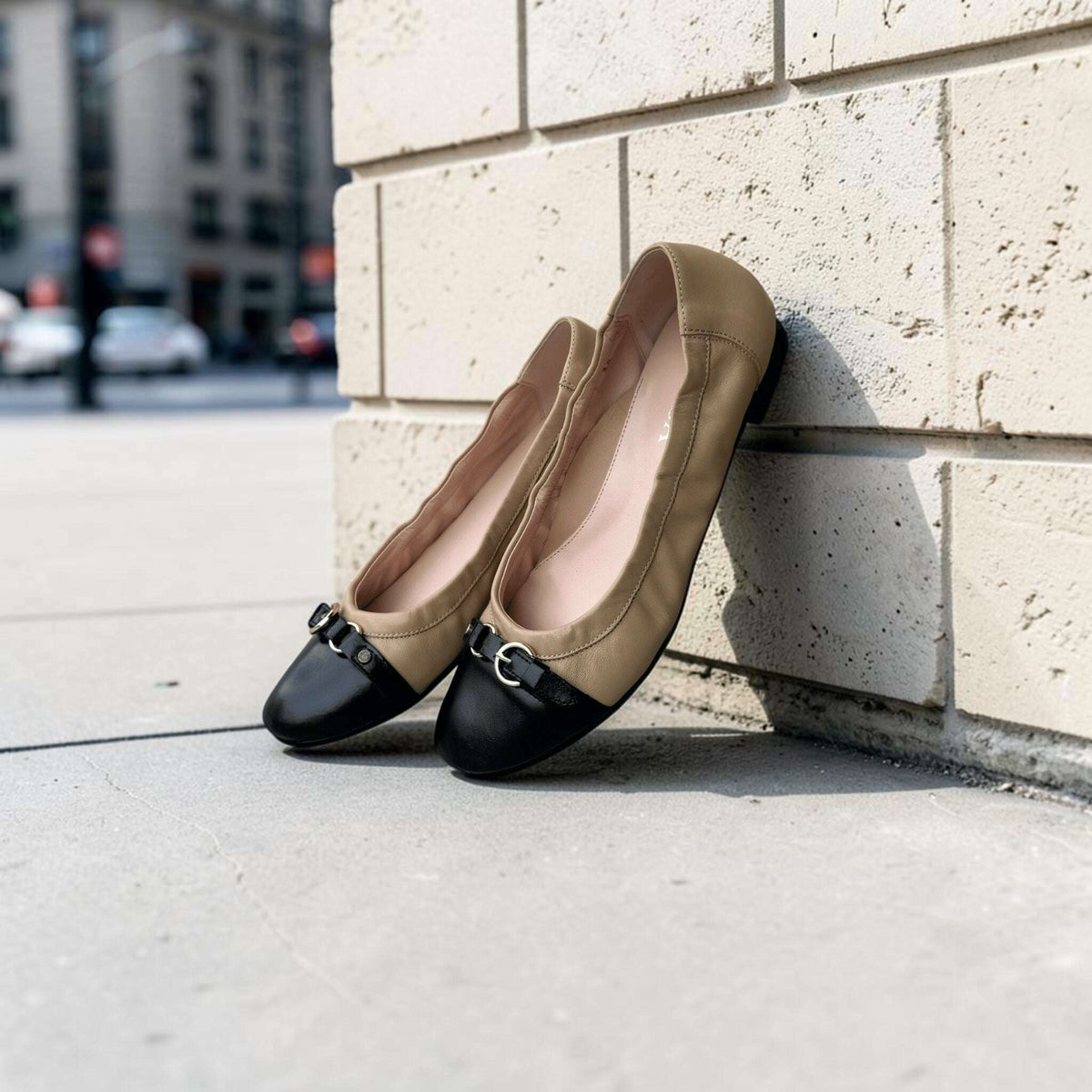 Plum Bottom LA LISA ballet flats in camel and black leather with a gold buckle detail leaning against a brick wall.
