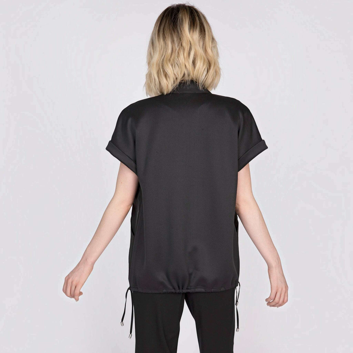 Back view of a woman wearing a black Plum Bottom mixed media vest with cuffed sleeves and a drawstring hem.