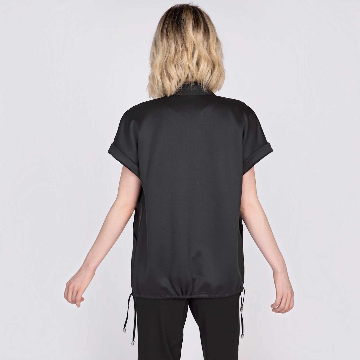 Back view of a woman wearing a black Plum Bottom mixed media vest with cuffed sleeves and a drawstring hem.