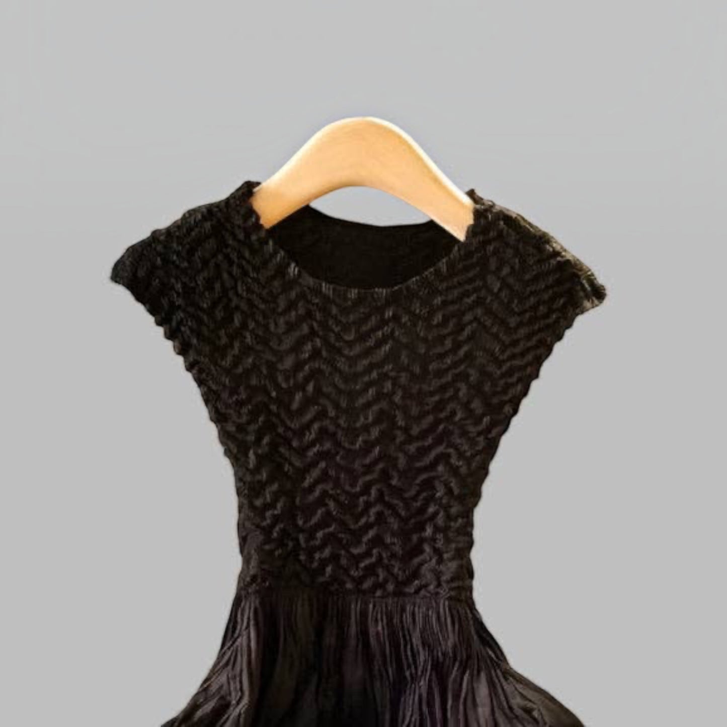 Plum Bottom Ellyndale black pleated dress with cupsleeves and textured bodice on a wooden hanger