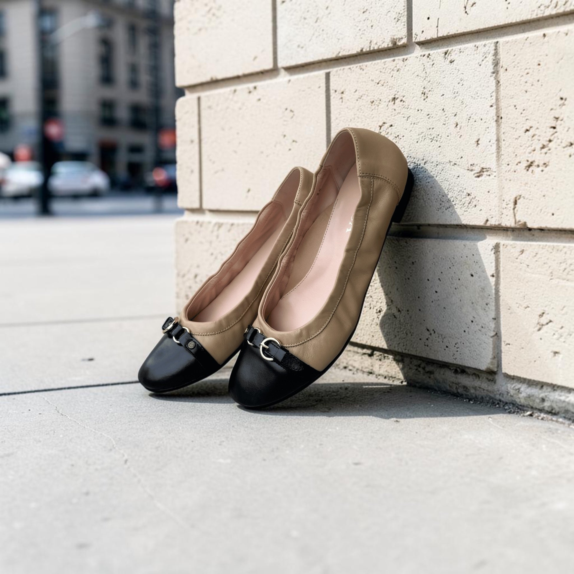 Plum Bottom LA LISA ballet flats in camel and black leather with a gold buckle detail leaning against a brick wall.