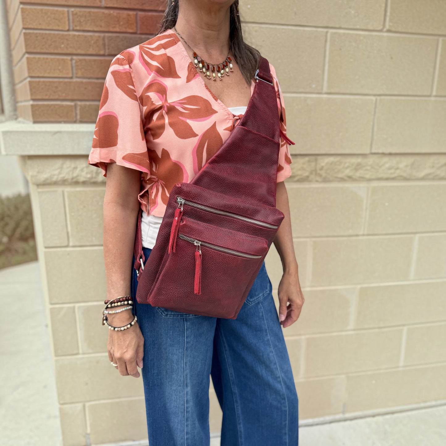 Plum Bottom DANIELLA LEHAVHI Ride sling bag in deep red pebbled leather worn crossbody by a woman in a floral top.