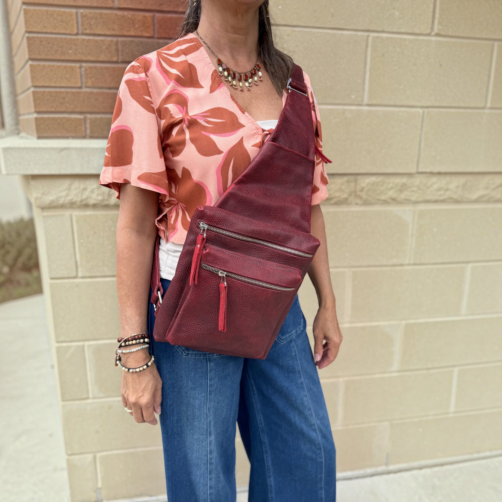 Plum Bottom DANIELLA LEHAVHI Ride sling bag in deep red pebbled leather worn crossbody by a woman in a floral top.