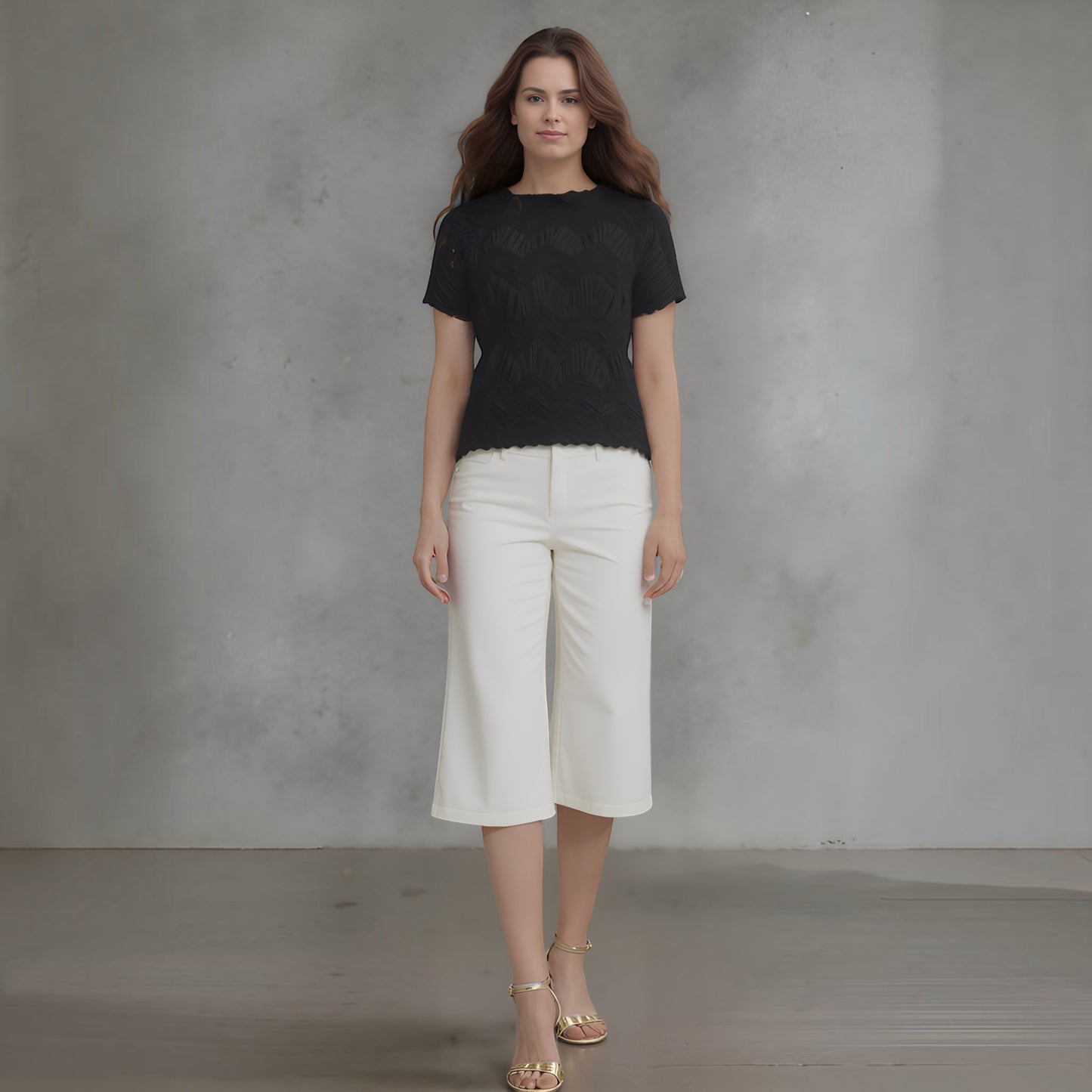 Plum Bottom model wearing a black Ellyndale short-sleeve top with crochet wave pleating and white cropped trousers.