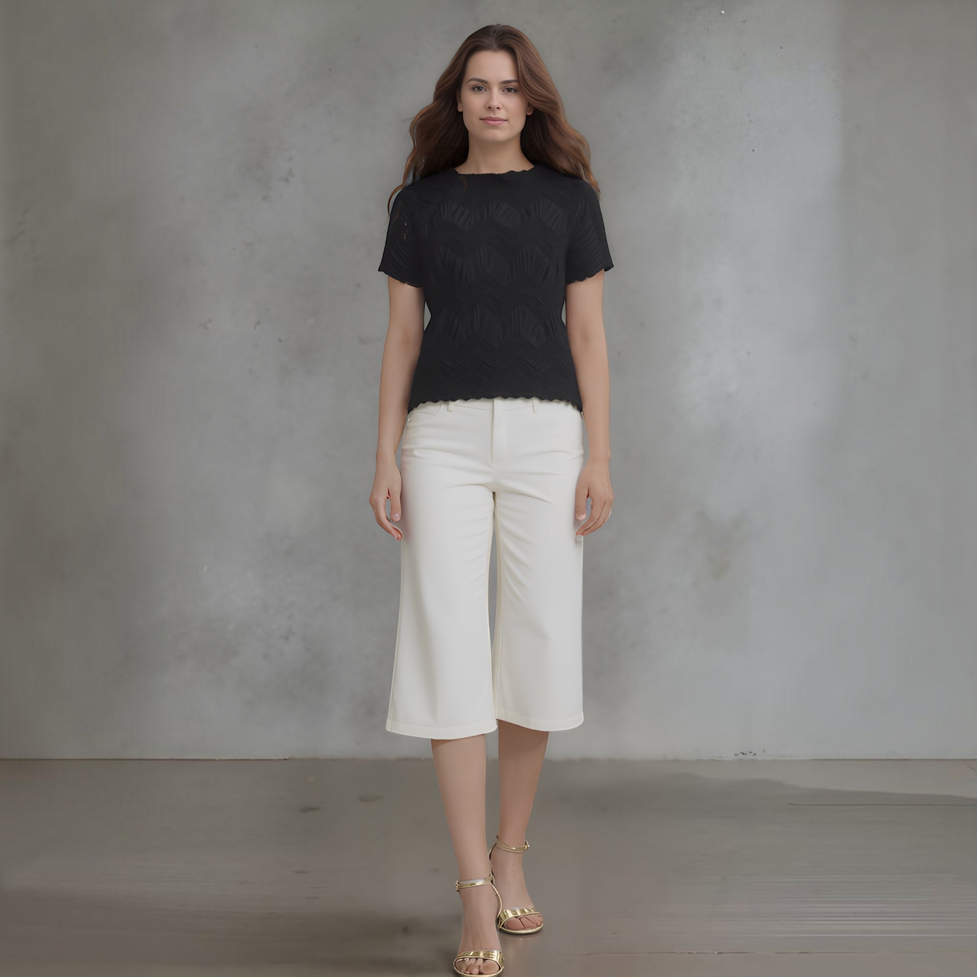 Plum Bottom model wearing a black Ellyndale short-sleeve top with crochet wave pleating and white cropped trousers.