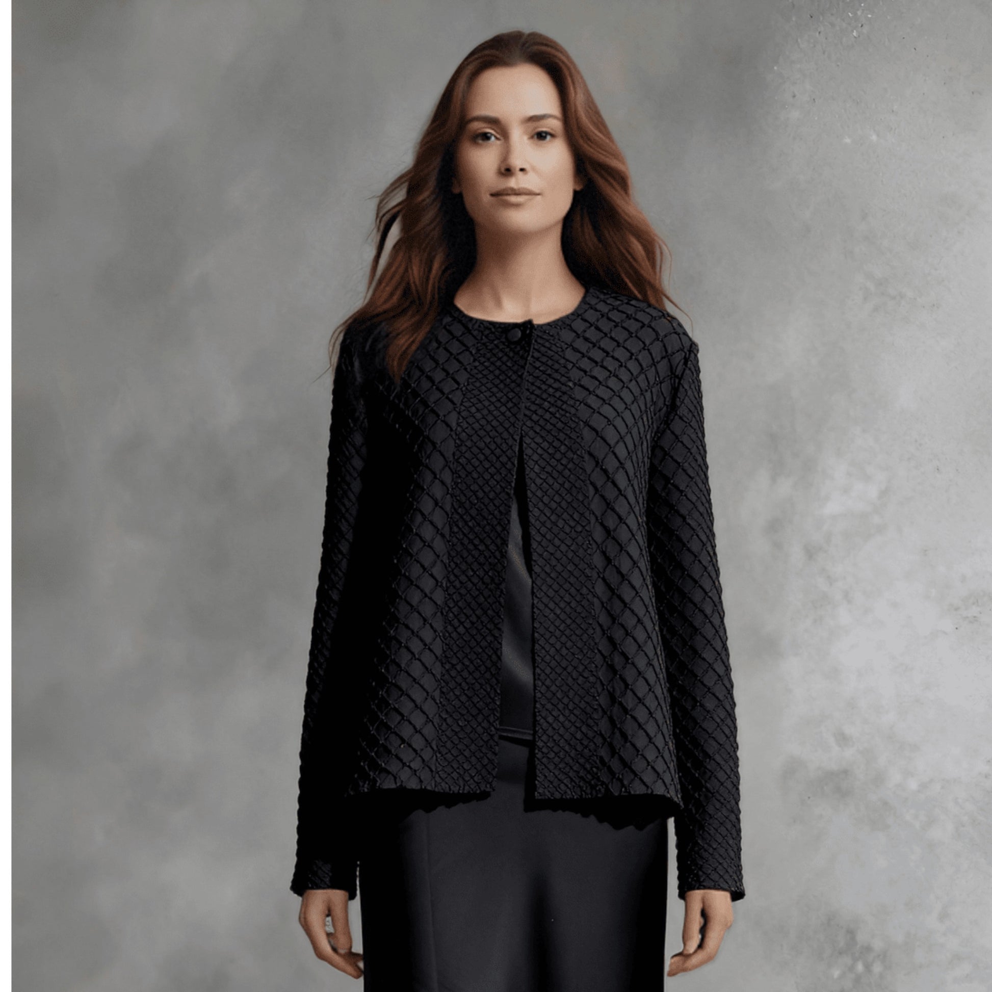 Plum Bottom ELLYNDALE black waffle weave pleated jacket with a round neckline and open front worn over a satin skirt.