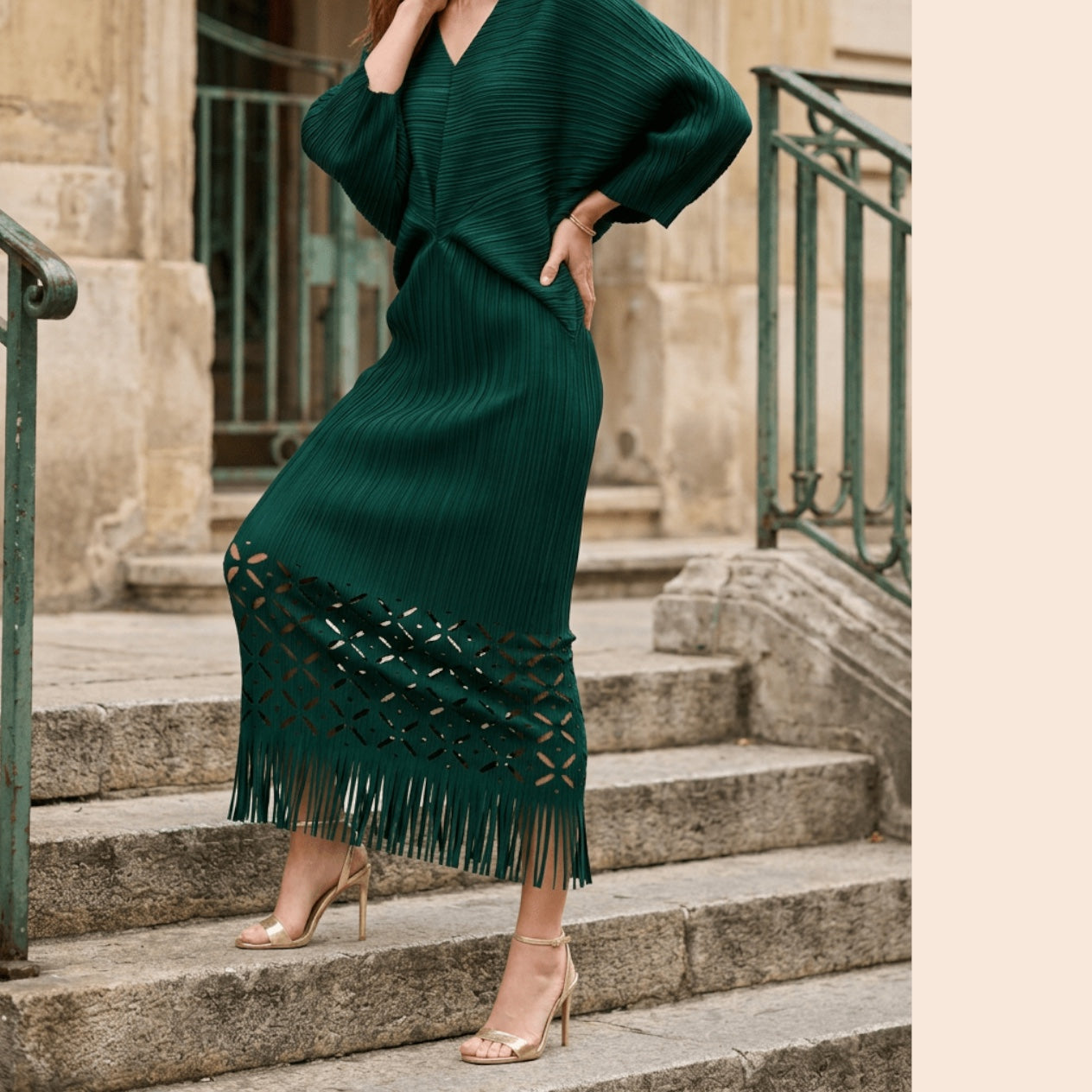 Plum Bottom ELLYNDALE dark green pleated midi dress with waist cutout, laser-cut hem, and fringe detail on stone steps