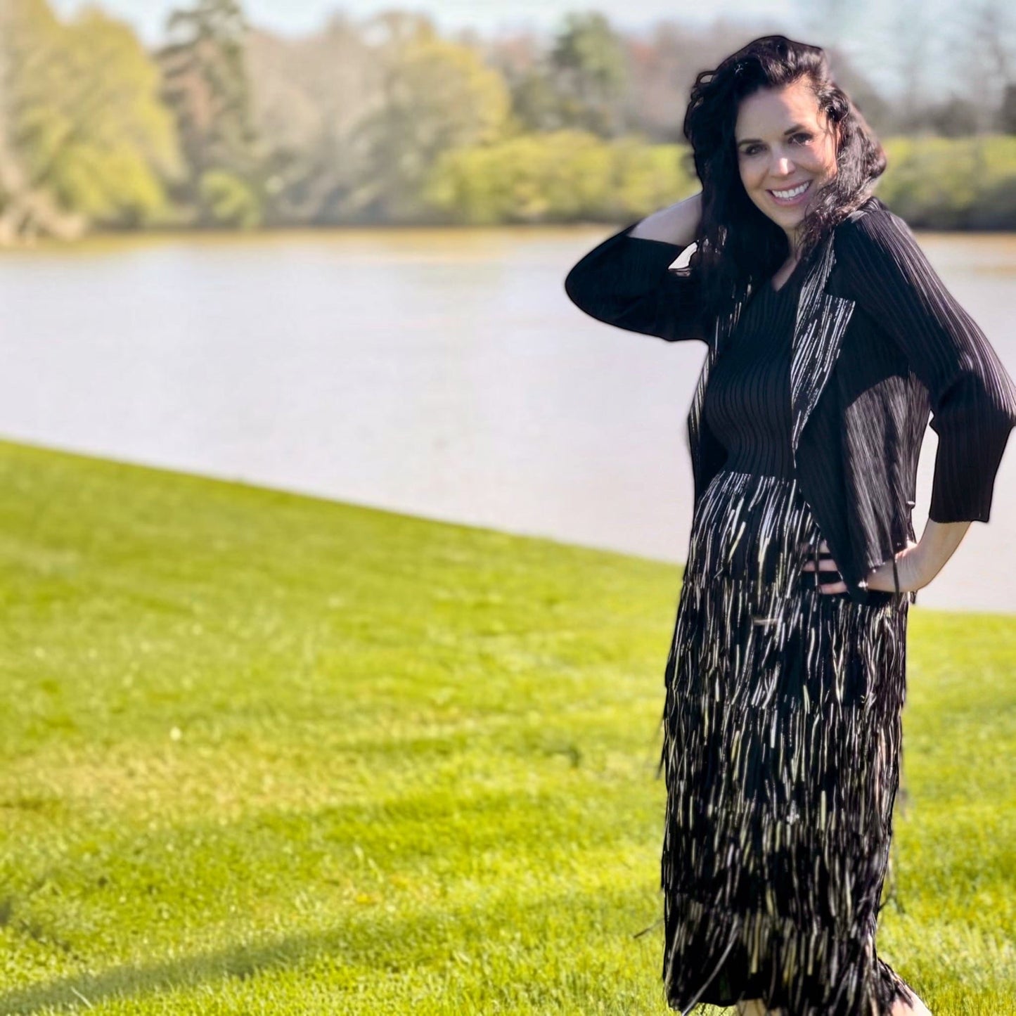 Plum Bottom Ellyndale black and gold pleated sleeveless dress and jacket set with fringe trim worn by a smiling woman
