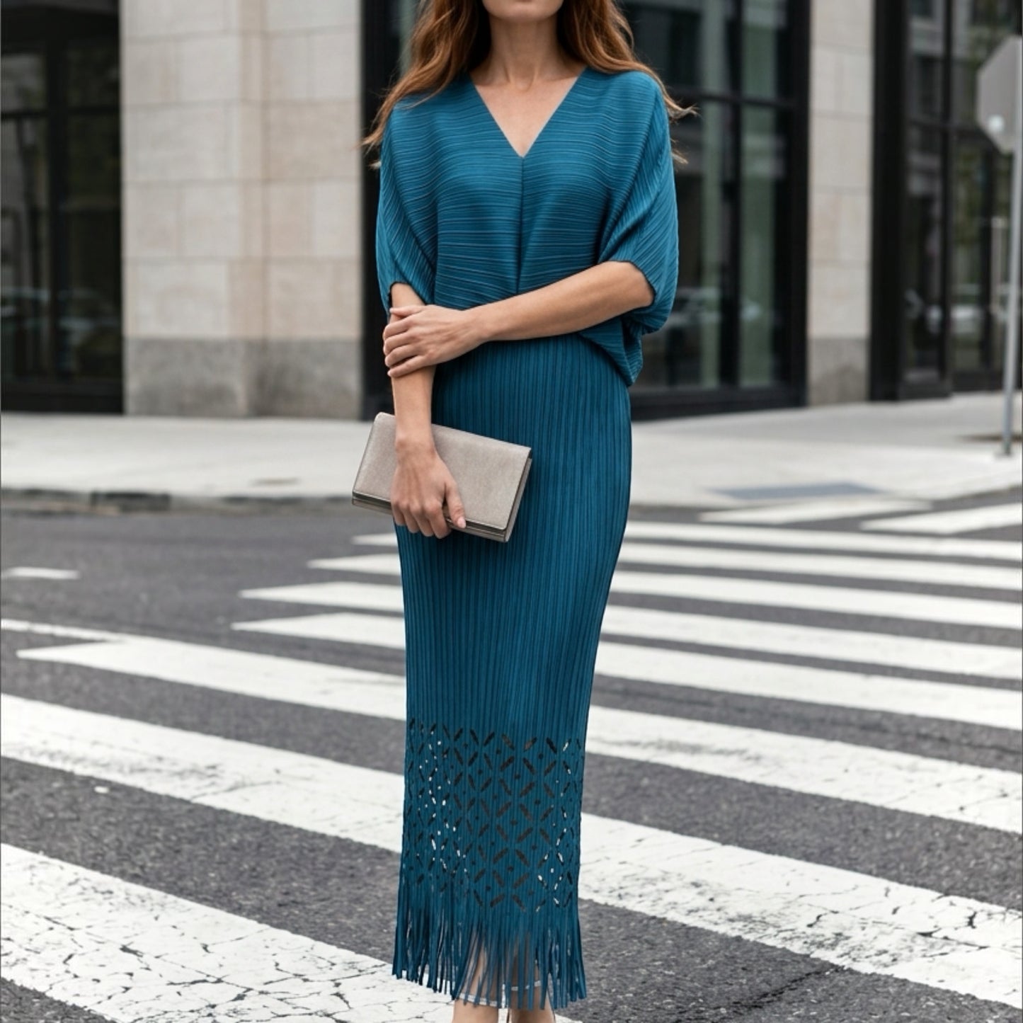 Plum Bottom teal pleated midi dress with waist cutout, laser-cut hem, and fringe detail worn on a city street.