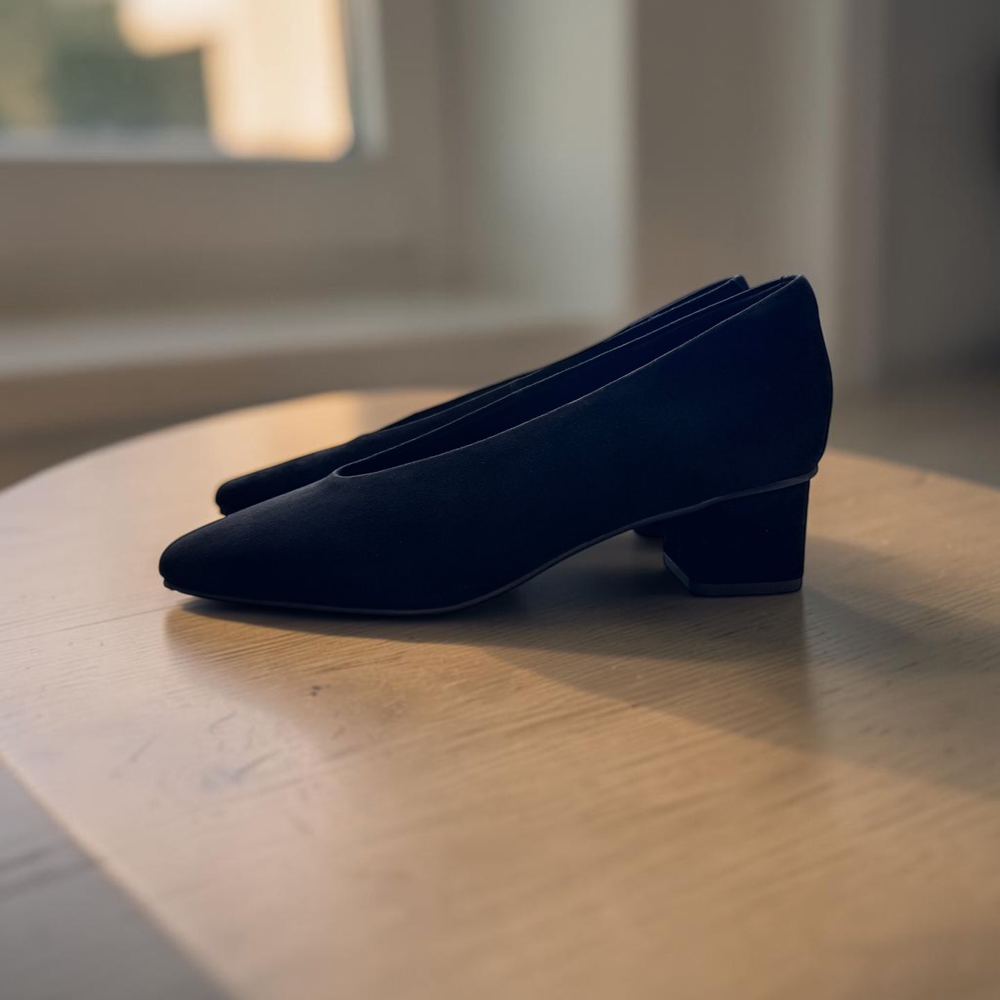 Plum Bottom VANELI Solara black suede pump with a square toe and block heel on a wooden table.