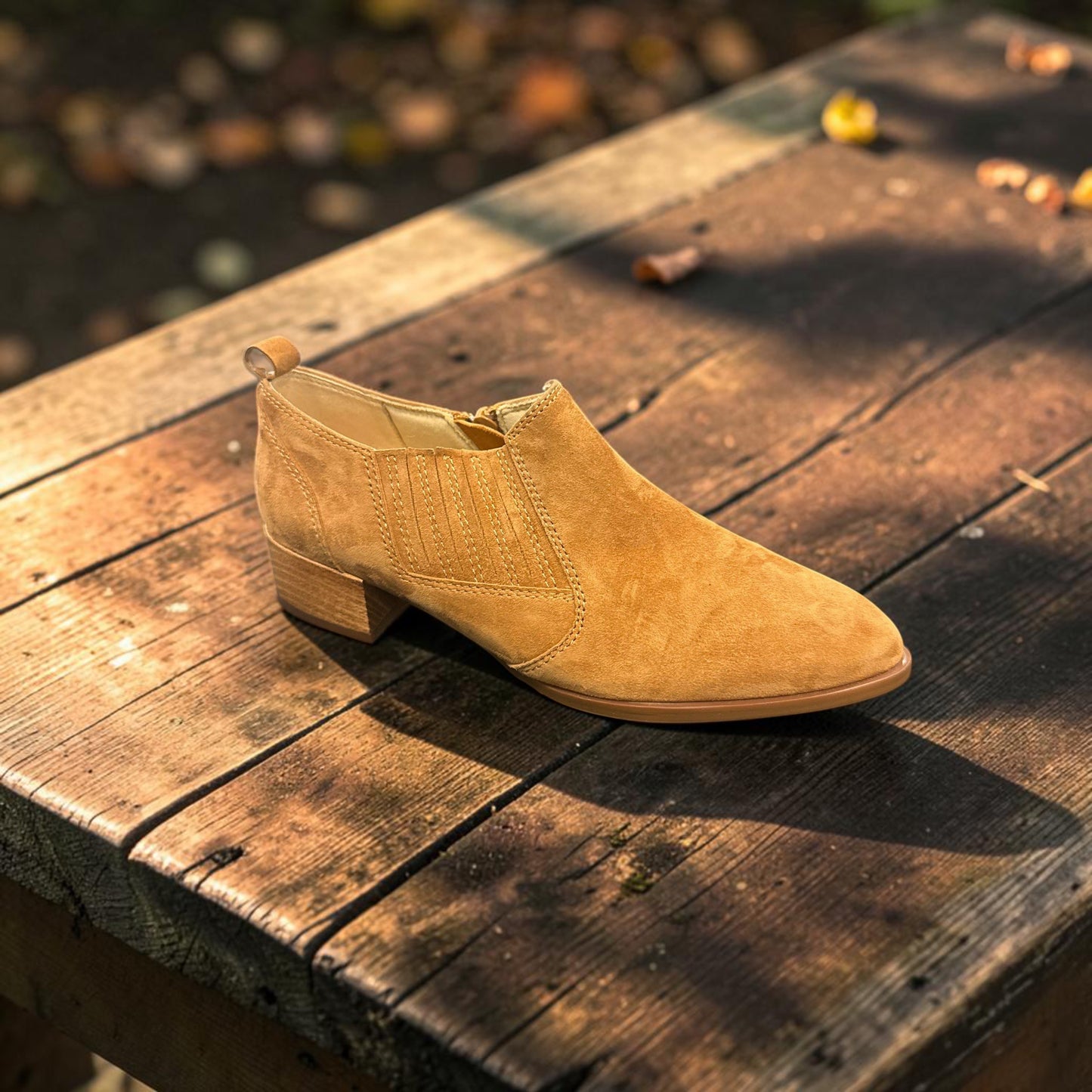 Plum Bottom VANELI Tess tan suede ankle bootie with side zipper and low block heel on a rustic wooden table