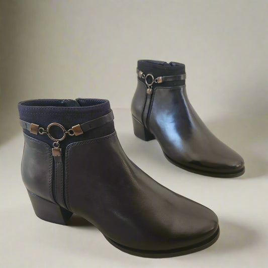 Pair of black leather boots with decorative rings on a beige floor.