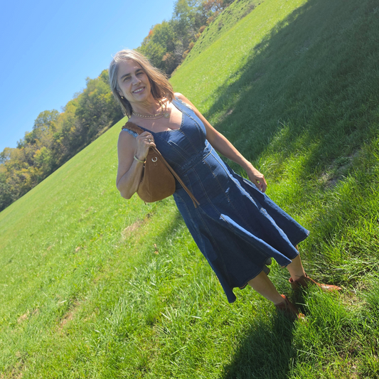 Plum Bottom sleeveless denim dress with heart-shaped bodice and hi-lo ruffled hem worn by a woman in a grassy field.