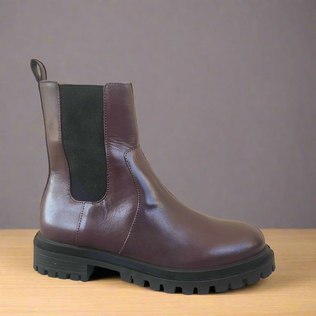 Brown leather boot with black sole on a beige tiled floor