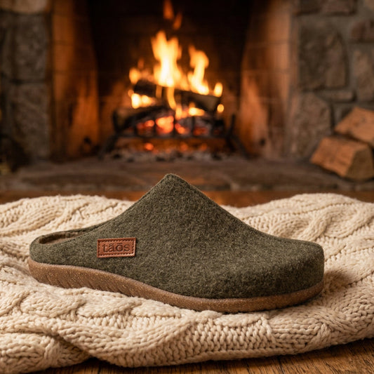 A single felt slip-on clog shoe in olive green with a brown sole, shown from a side profile on a white background. A small brown leather brand patch on the heel reads 'taos'.