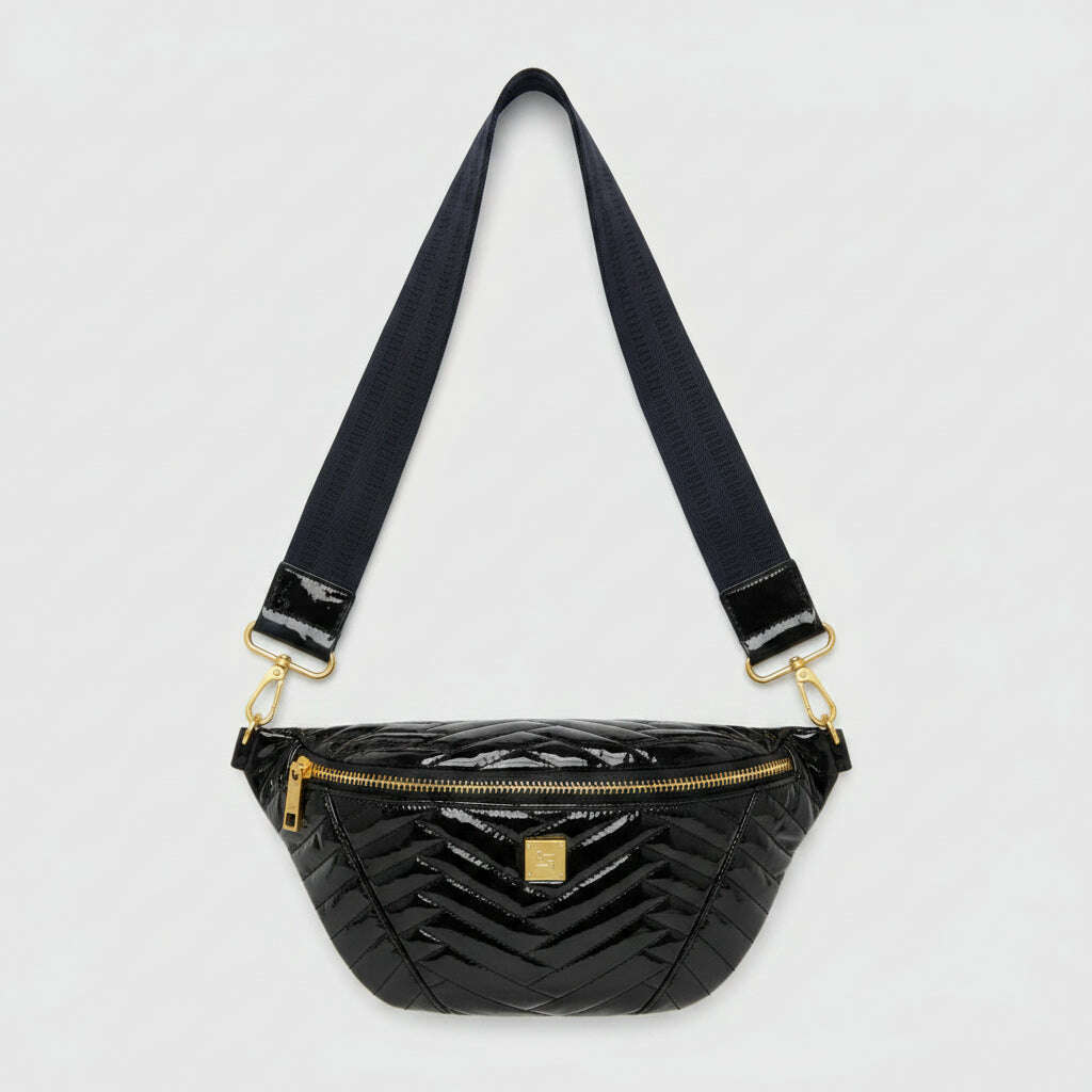 A glossy black chevron-patterned patent leather fanny pack with a wide navy blue strap and gold-tone hardware, resting on a beige fabric surface.