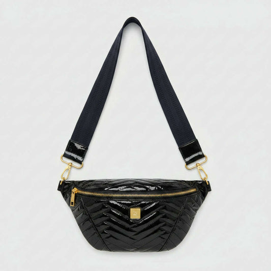 A glossy black chevron-patterned patent leather fanny pack with a wide navy blue strap and gold-tone hardware, resting on a beige fabric surface.