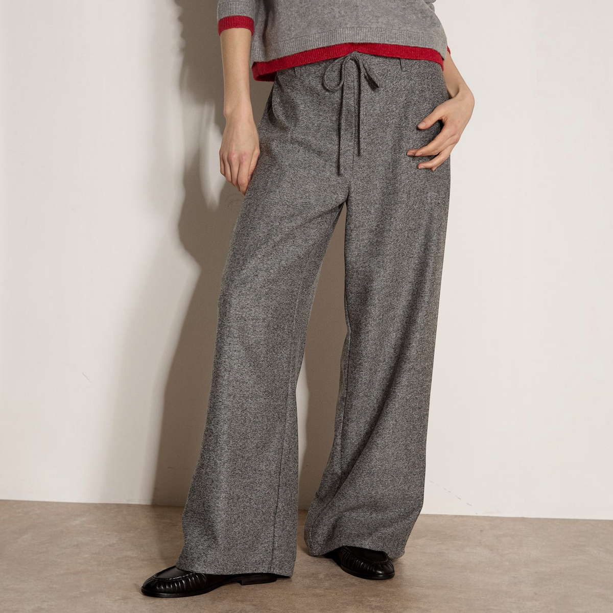 Plum Bottom grey tweed trousers with a tie-front closure and wide-leg fit, styled with a red-trimmed grey sweater.