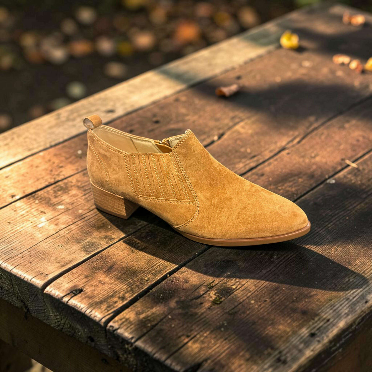 Plum Bottom VANELI Tess tan suede ankle bootie with side zipper and low block heel on a rustic wooden table